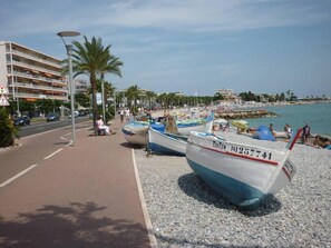 A beachside scene with boats, a pedestrian path, and a building in the background. - F2 ON THE GROUND FLOOR 150m from the beaches and shops / 5pers / 48m2 (Cagnes-Sur-Mer)