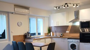 A modern kitchen with a dining area, featuring a chandelier, built-in appliances, and a clock on the wall. - F2 ON THE GROUND FLOOR 150m from the beaches and shops / 5pers / 48m2 (Cagnes-Sur-Mer)
