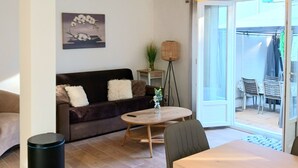A living room with a sofa, a coffee table, a dining table, and a trash bin. - F2 ON THE GROUND FLOOR 150m from the beaches and shops / 5pers / 48m2 (Cagnes-Sur-Mer)
