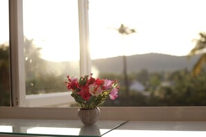 A vase with flowers on a windowsill, with a view of mountains and a bird flying in the background. - Purple Place Homestay - Hostel (Phu Quoc)