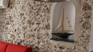 A room with a stone wall, a red sofa, a wooden table, and a model ship. - CHARMING STUDIO - HEART OLD TOWN OF ANTIBES NEAR THE SEA AND OUT (Antibes)