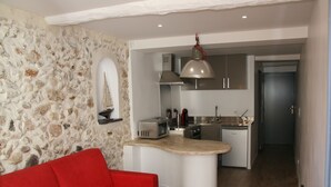 A modern kitchen with a central island, a red sofa, and a stone wall. - CHARMING STUDIO - HEART OLD TOWN OF ANTIBES NEAR THE SEA AND OUT (Antibes)