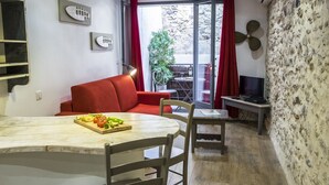 A living room with a red sofa, a dining table with a plate of food, a TV, and a stone wall. - CHARMING STUDIO - HEART OLD TOWN OF ANTIBES NEAR THE SEA AND OUT (Antibes)