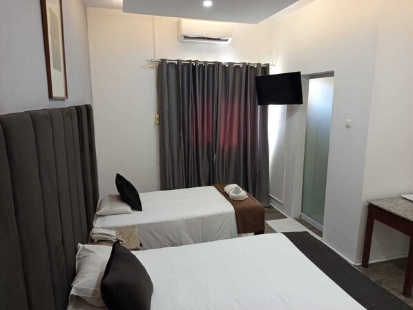A hotel room with two beds, a flat-screen TV mounted on the wall, a small table, and a sliding door leading to a bathroom.