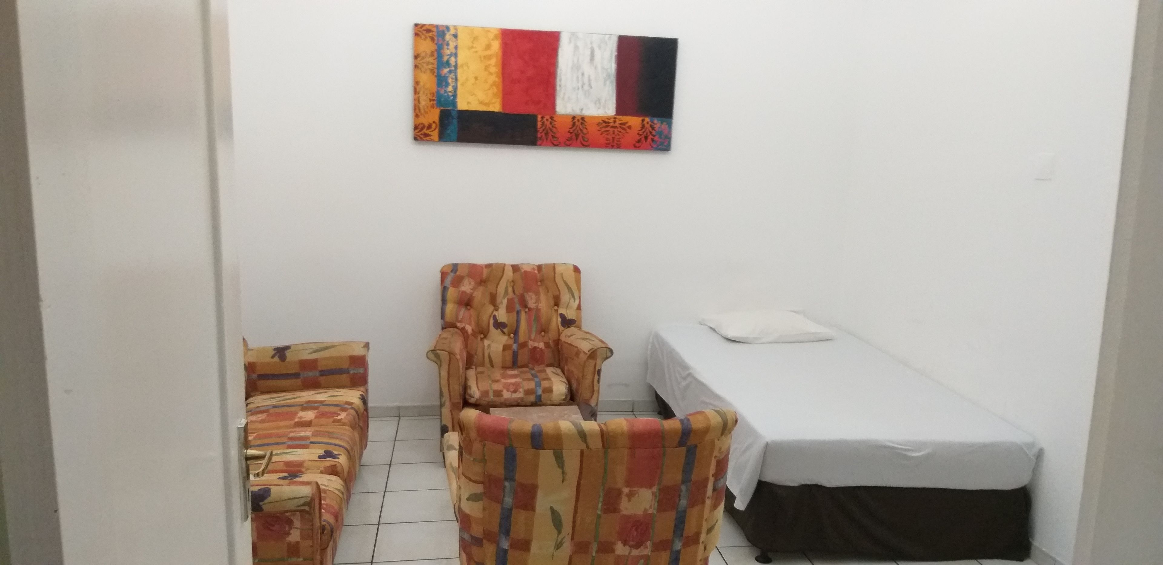 A small, compact room with a sofa, a chair, and a single bed.