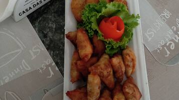 Um prato retangular com alimentos fritos, incluindo croquetes e samosas, guarnecido com alface e uma fatia de tomate.