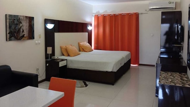 Quarto de hotel com cama, escrivaninha, cadeira, televisão e ar condicionado.