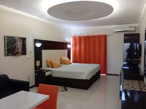 Habitación de hotel con cama, escritorio, silla, televisión y aire acondicionado.