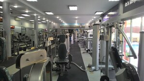 Uma academia com diversos aparelhos de exercício, espelhos e uma frase motivacional na parede.