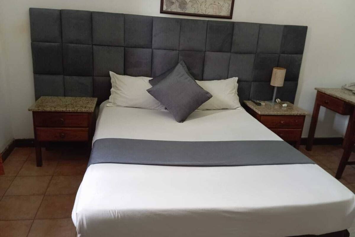 Una cama con cabecera capitonada, dos mesitas de noche y una mesita auxiliar con lámpara.