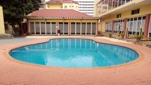 Piscina com borda de tijolos, cercada por um edifício com janelas amplas e telhado vermelho.