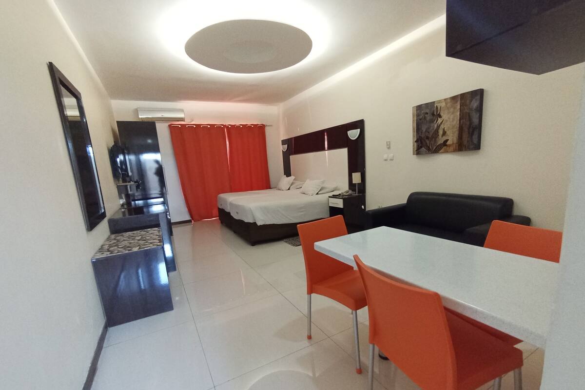 Una habitación de hotel moderna con una cama, un sofá, una mesa de comedor con sillas, un televisor y un cuadro en la pared.