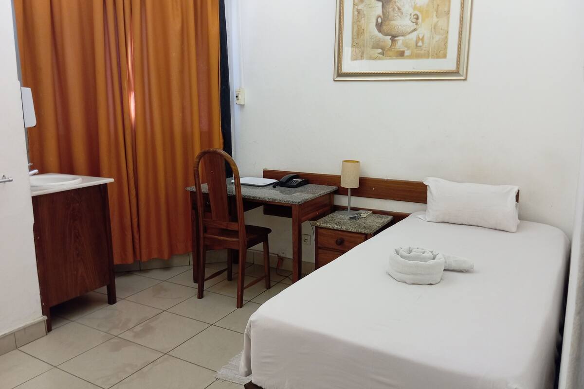 Habitación de hotel con una cama, un escritorio con silla, un teléfono, una lámpara y un cuadro en la pared.