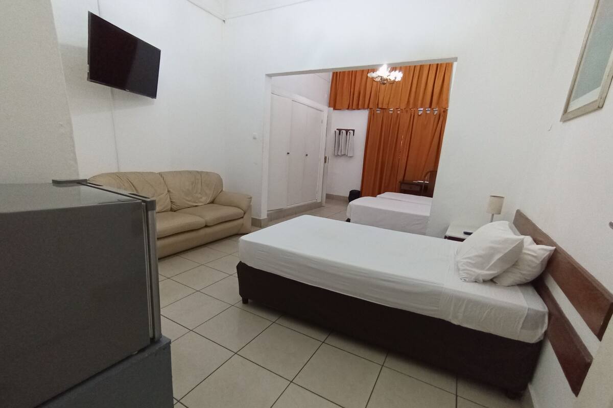 Habitación de hotel compacta con cama, sofá, televisión y refrigerador.