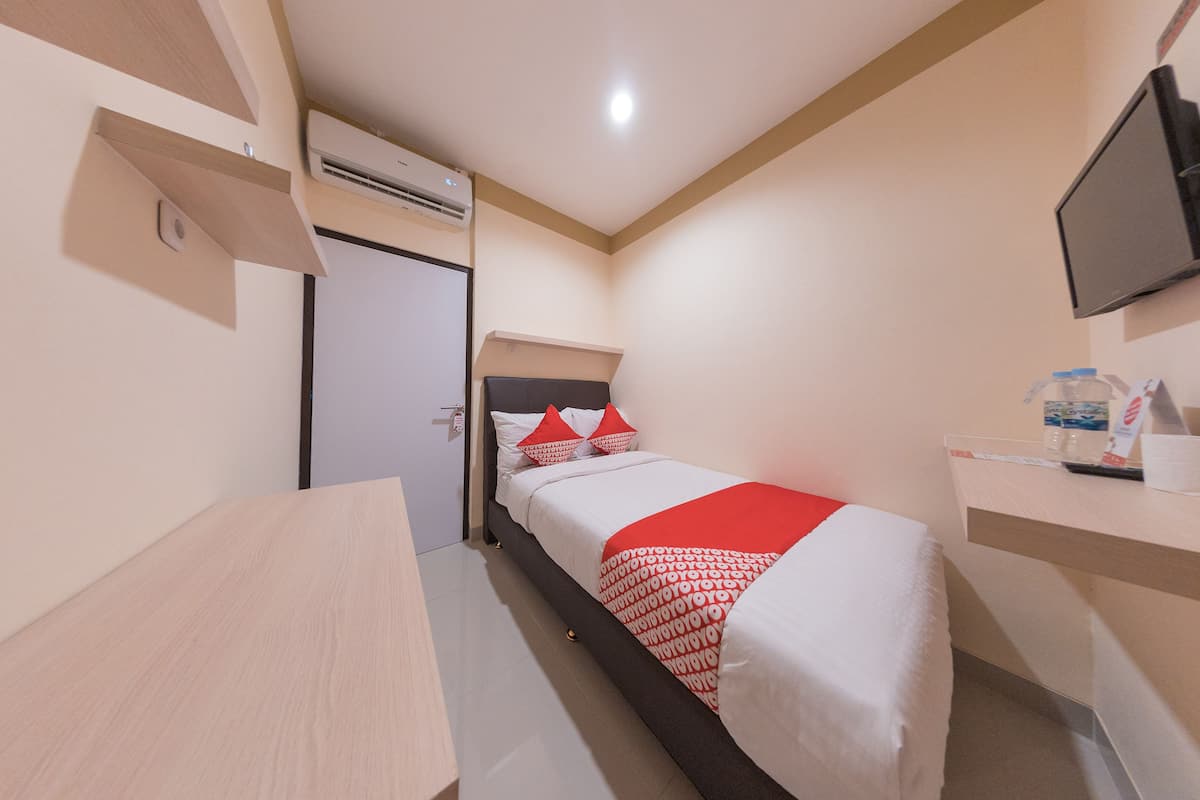 A compact hotel room with a bed, a desk, a TV, and a water dispenser.