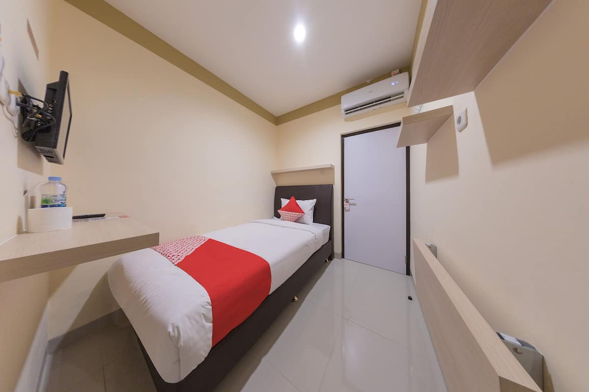 A small, neatly arranged bedroom with a bed, a bedside table, an air conditioning unit, and a door.