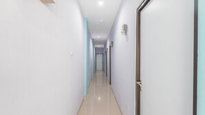 A long, narrow hallway with light-colored walls and a tiled floor. - Hotel O Balcon Biru (Jakarta)