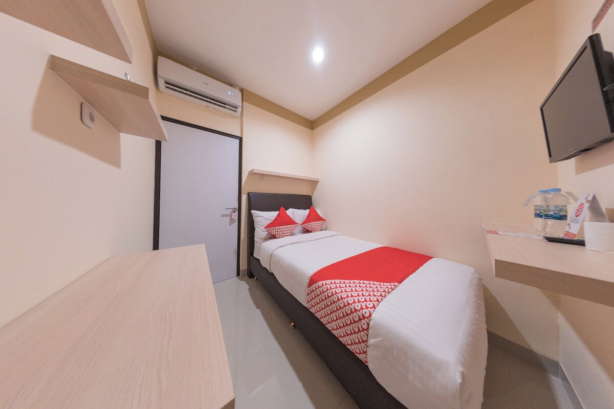 A compact hotel room with a bed, a desk, a TV, and a water dispenser.