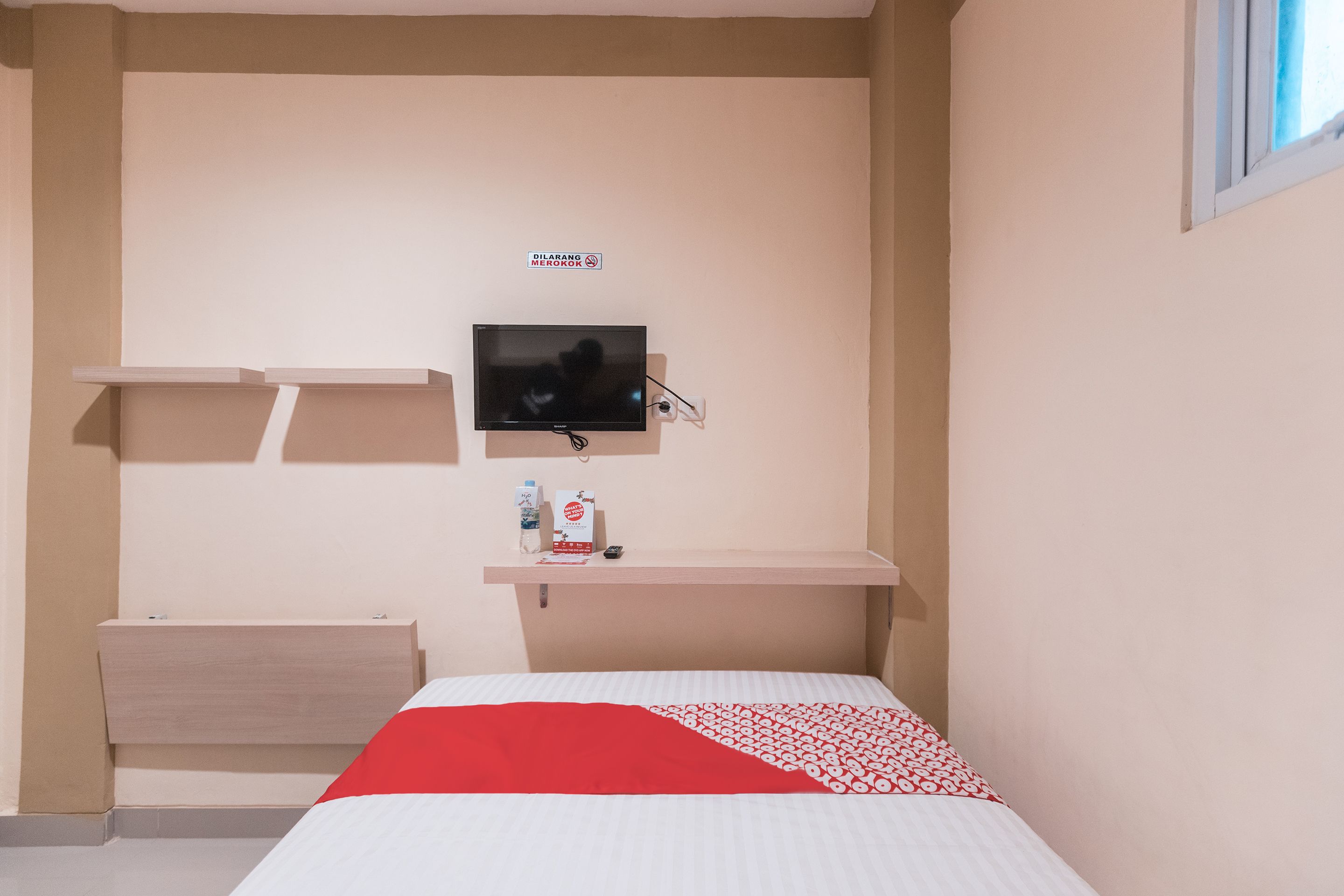 Une chambre d’hôtel avec un lit, un téléviseur fixé au mur, un petit bureau et une étagère.