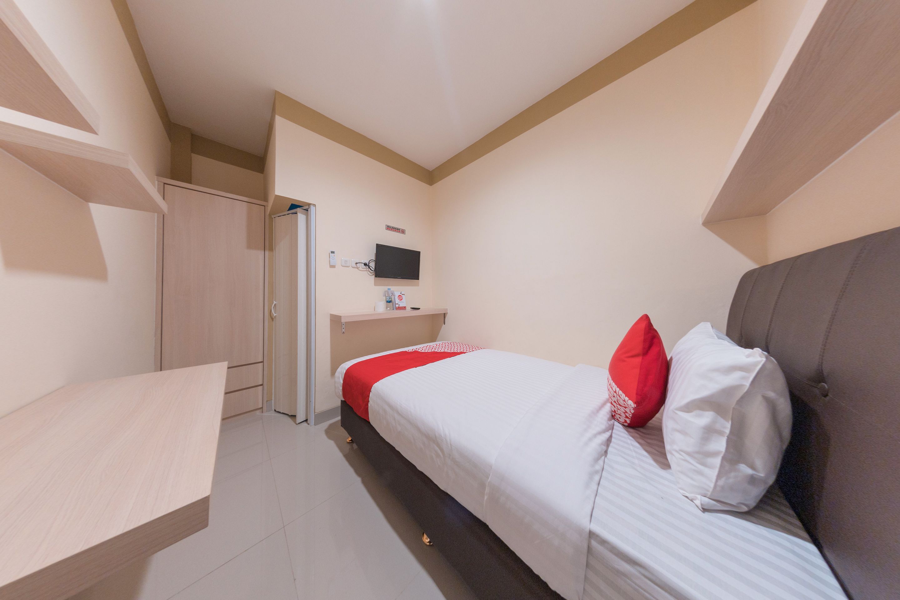 A hotel room with a bed, a desk, a wardrobe, and a television on the wall.
