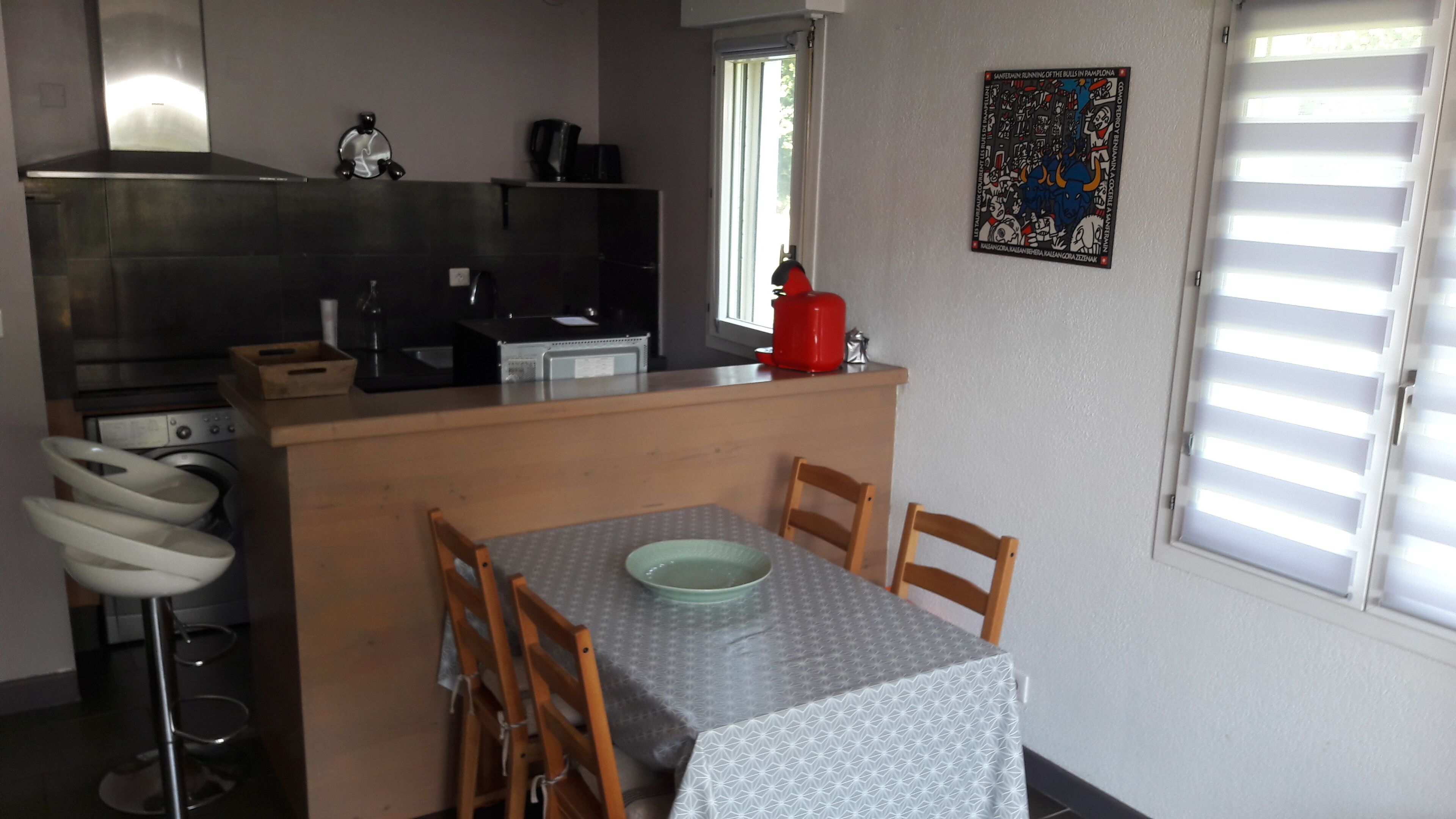 Une cuisine compacte avec un coin repas, comprenant une table avec des chaises, un lave-linge et une bouilloire rouge.