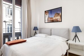 Ein Hotelzimmer mit einem Bett, zwei Nachttischlampen, einem Fenster mit Vorhängen und einem gerahmten Bild an der Wand.