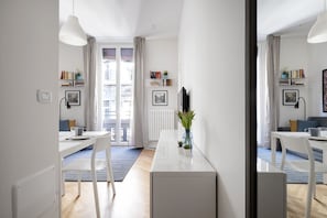 A modern, well-lit room with a dining table, chairs, a white cabinet, and a large window with curtains.