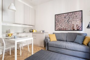 Eine moderne Küche mit weißen Schränken, einem Esstisch und einem grauen Sofa mit gelben Kissen.