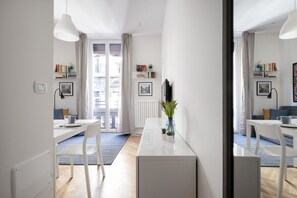 Una habitación moderna y bien iluminada con una mesa de comedor, sillas, un armario blanco y un ventanal con cortinas.