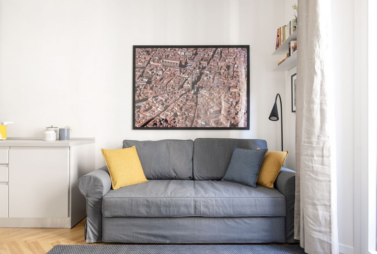 A modern living room with a grey sofa, a framed cityscape picture, a small white cabinet, and a black floor lamp.