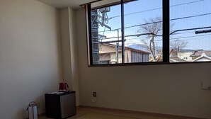 A room with tatami flooring, a small heater, and a window overlooking a residential area. - Machi no Hotel (Fujiyoshida)