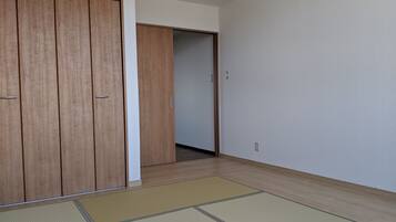 A room with a wooden wardrobe, a sliding door, tatami mats on the floor, and a plain wall.