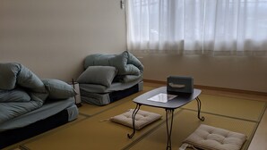 A traditional Japanese-style room with tatami flooring, a low table with a laptop, and cushions on a sofa. - Machi no Hotel (Fujiyoshida)