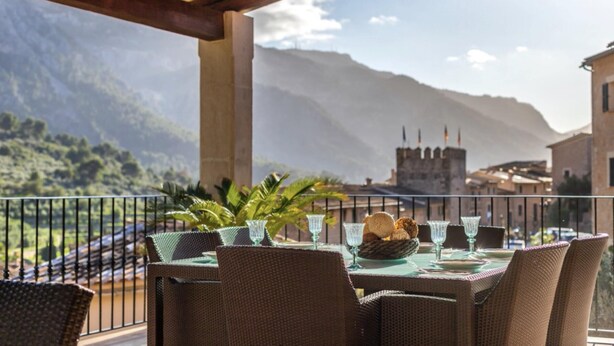 A table set outdoors with wicker chairs, a glass table, and a view of mountains and a castle. - VILLA CIRCE - Exclusive villa with indoor heated pool in Fornalutx. (fornalutx)