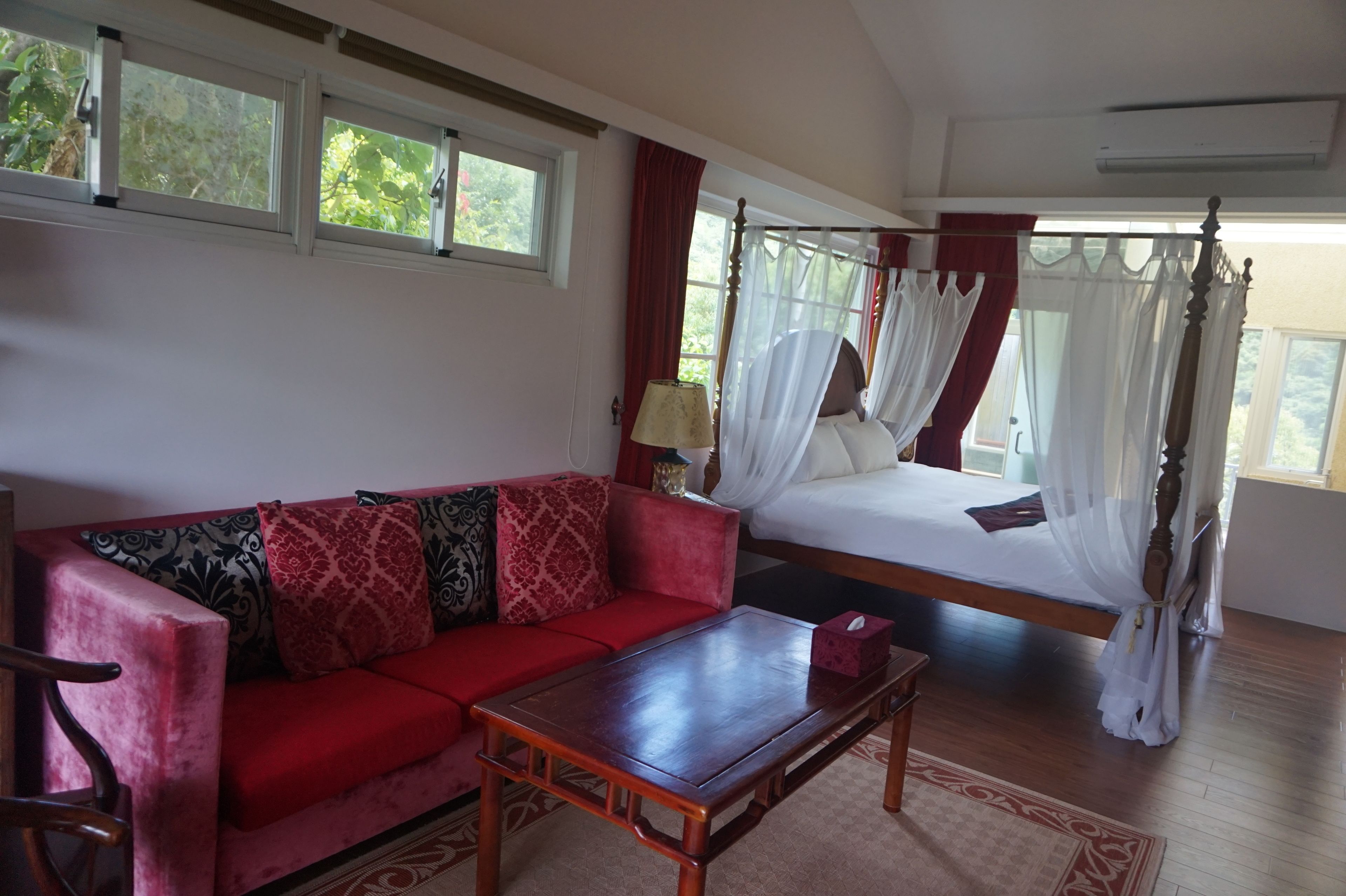 A bedroom with a four-poster bed, a red sofa, and a wooden coffee table.