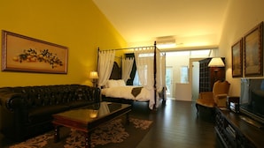 A room with a four-poster bed, a leather sofa, a coffee table, and a television. - Juhu Farmstay (Changbin)