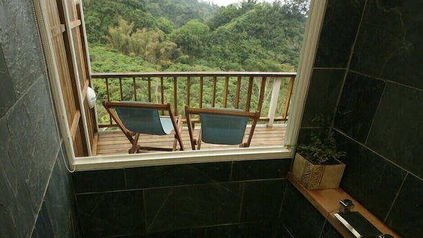 A bathroom with a wooden bathtub, a window with a view of a forest, and two chairs on a balcony. - Juhu Farmstay (Changbin)