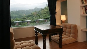 A room with a wooden table, two plush armchairs, a bookshelf, and a view of a mountainous landscape through a large window. - Juhu Farmstay (Changbin)