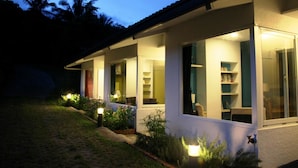 A house with a covered porch, large windows, and a well-lit interior. - Juhu Farmstay (Changbin)