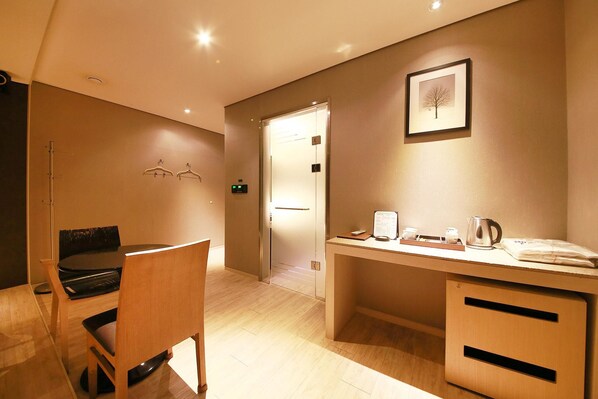 Habitación de hotel con un escritorio de madera, una silla, una cama y una puerta que da al baño.