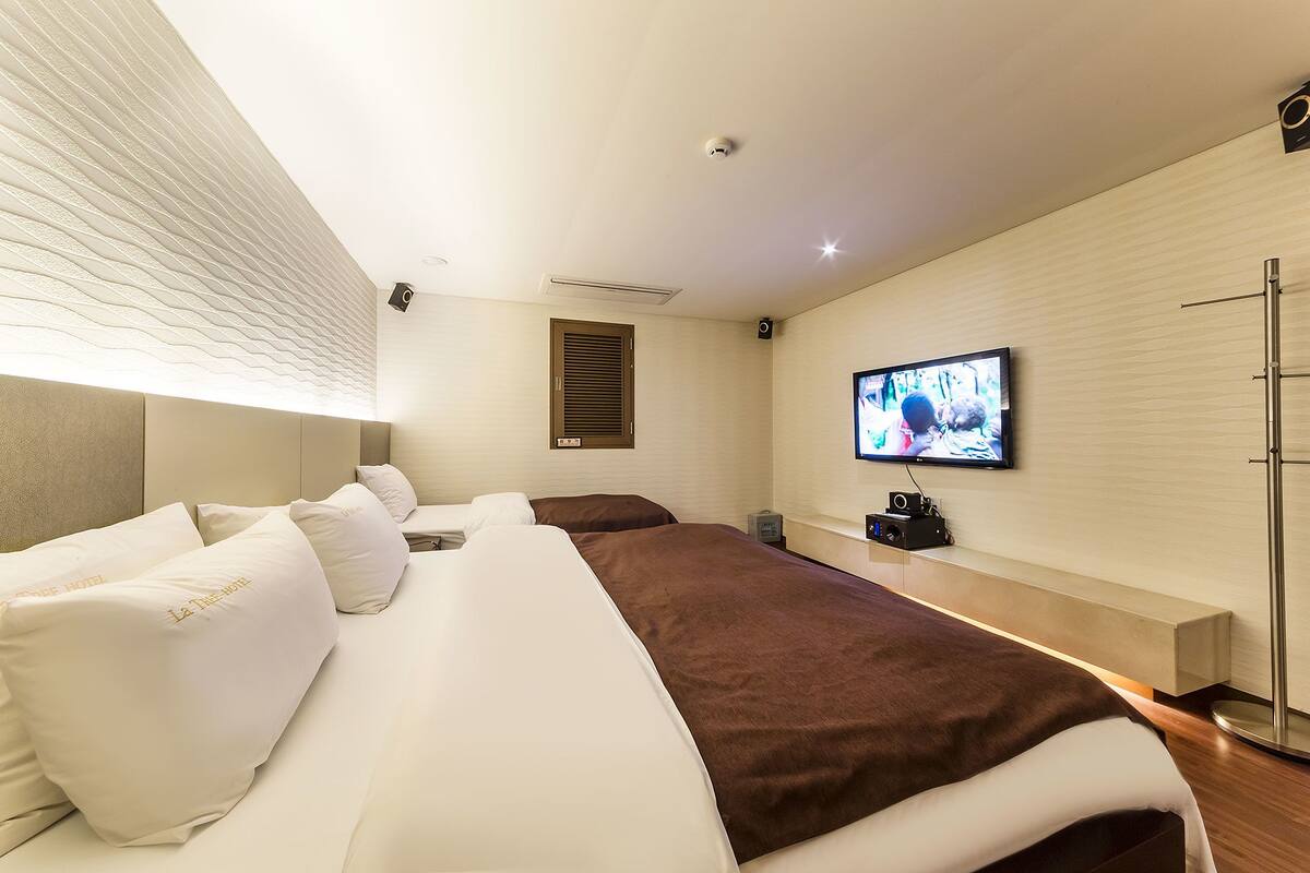 A modern hotel room with a large bed, a television mounted on the wall, and a ceiling-mounted security camera.
