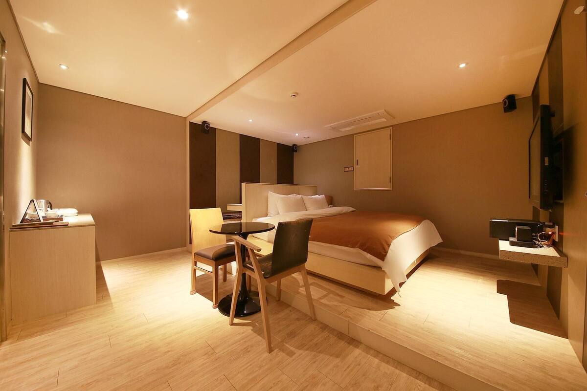 A modern hotel room with a bed, a desk, a chair, and a TV.