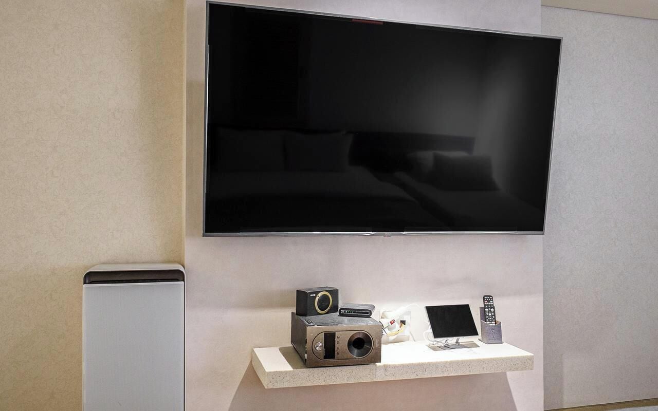 Un televisor de pantalla plana montado en la pared, una mesita con una cámara, un control remoto y una caja pequeña.