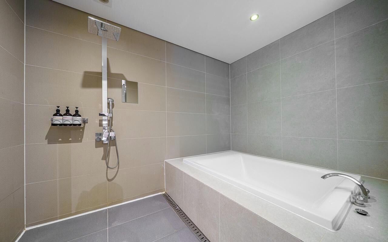 A modern bathroom with a bathtub, a shower, and a wall-mounted soap dispenser.