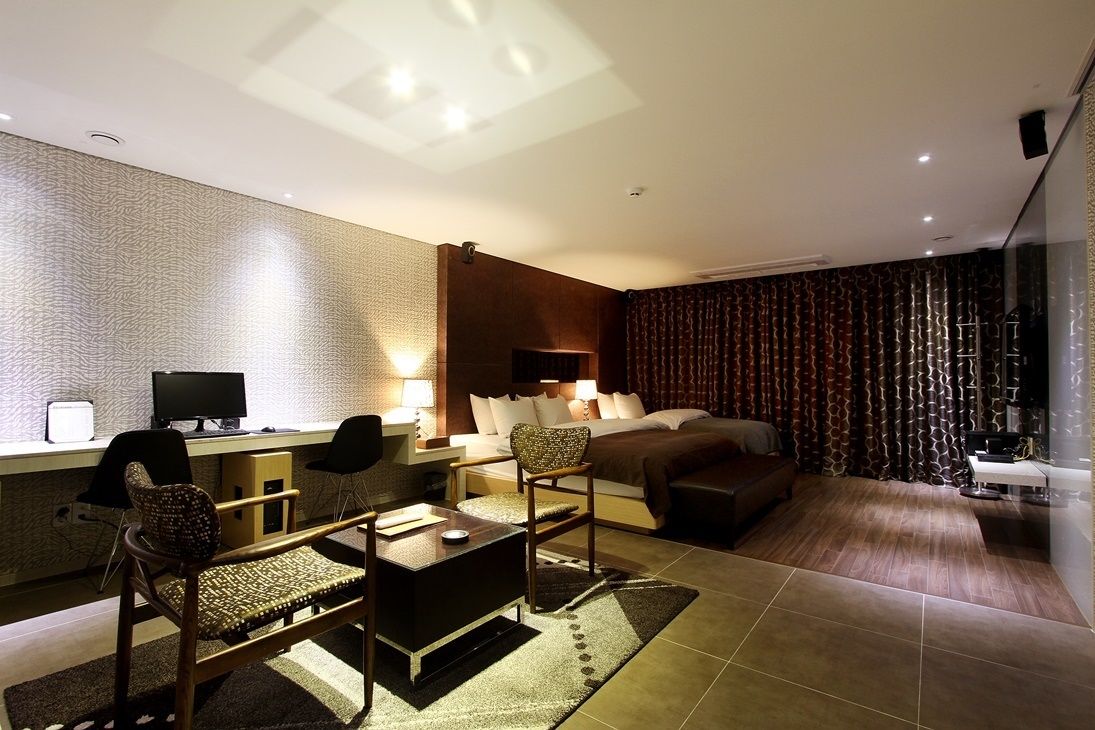 Une chambre d’hôtel moderne équipée d’un bureau, de deux chaises, d’un lit avec une tête de lit, d’une table de chevet et d’une grande fenêtre avec des rideaux.
