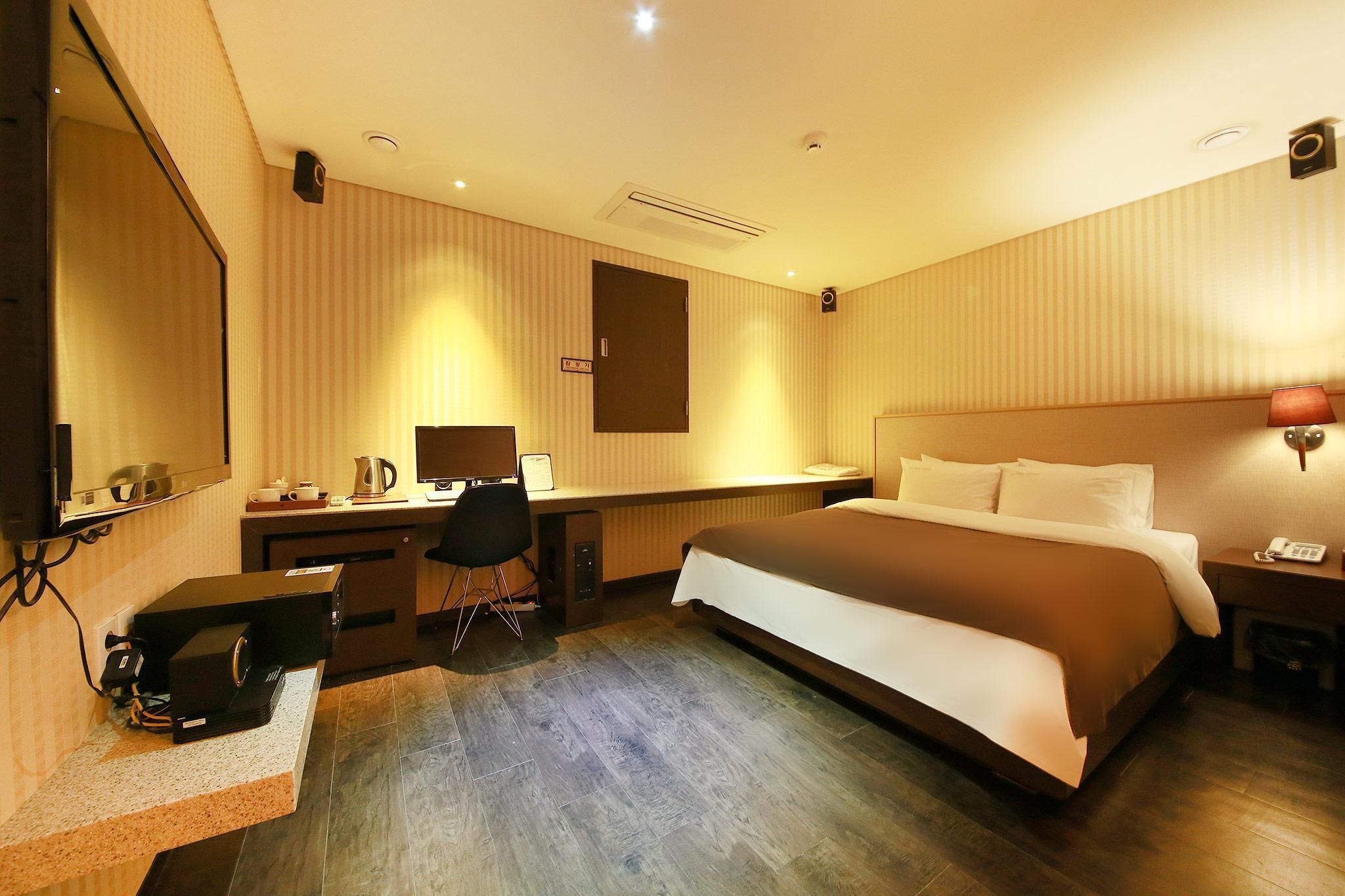 A hotel room with a large bed, a desk with a computer, a chair, a coffee maker, and a TV.