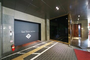 Entrada de un hotel con un letrero que dice "La Tree HOTEL" y un extintor a la izquierda.