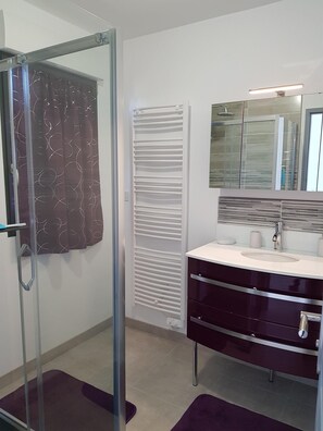 Une salle de bain moderne avec une douche à parois de verre, un meuble-lavabo avec miroir et un porte-serviettes.