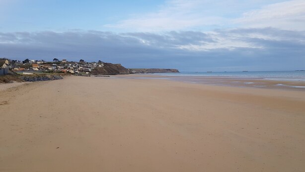 A wide sandy beach with a calm sea and a distant town.