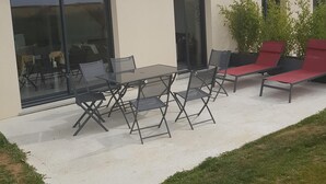 A modern building with a flat roof, large sliding glass doors, and a patio area with outdoor furniture.